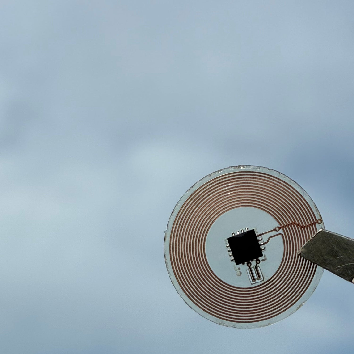Small electronic component held by tweezers with a blurred sky background